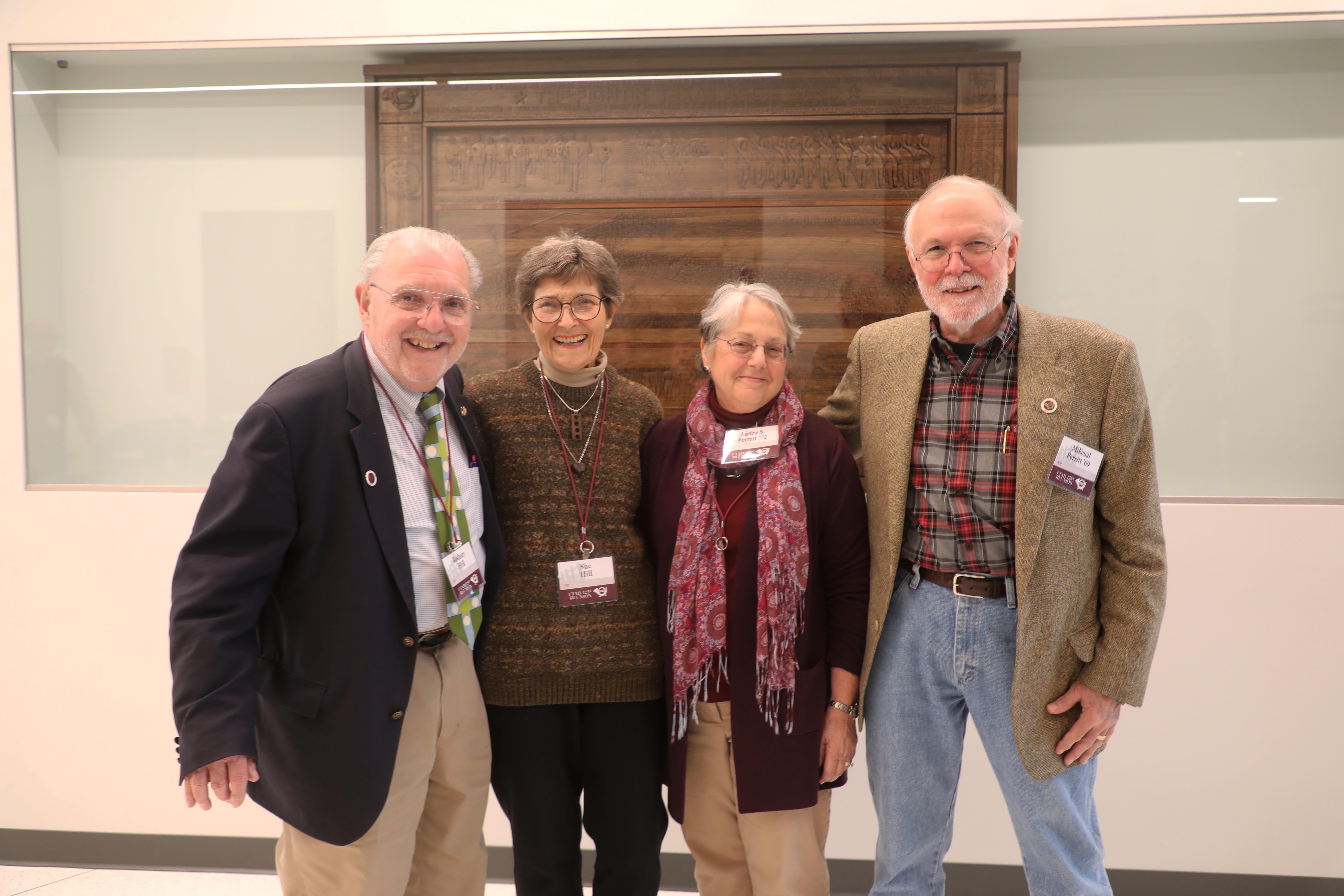 Rodney Hill, Sue Hill, Laura Perritt and Mikeual Perritt stand in front of the wood panel honoring the history of the Texas A&M Fightin’ Aggie Band displayed in the Music Activities Center. 